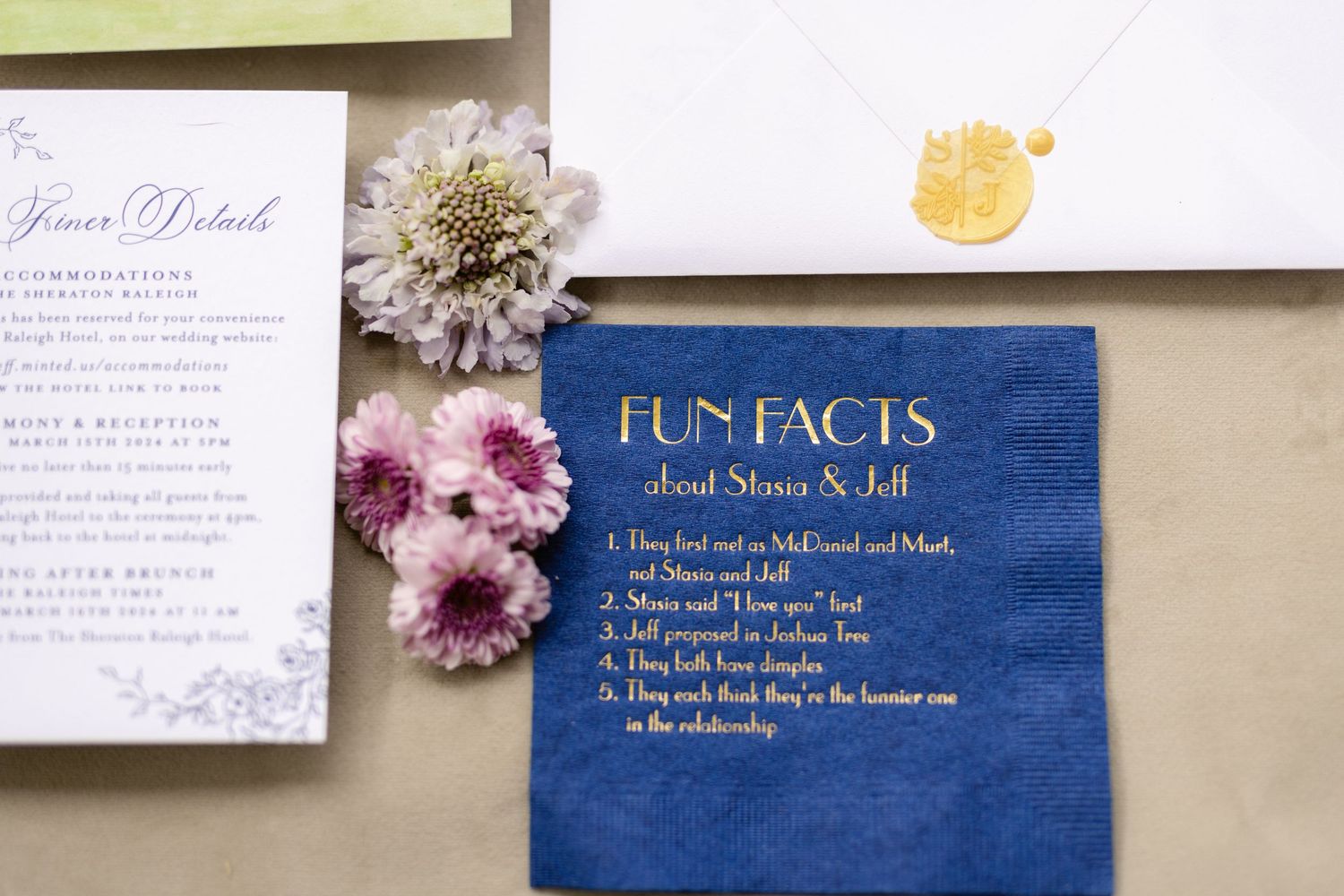 A navy blue fun facts wedding card displayed alongside dried flowers and wedding invitation details.