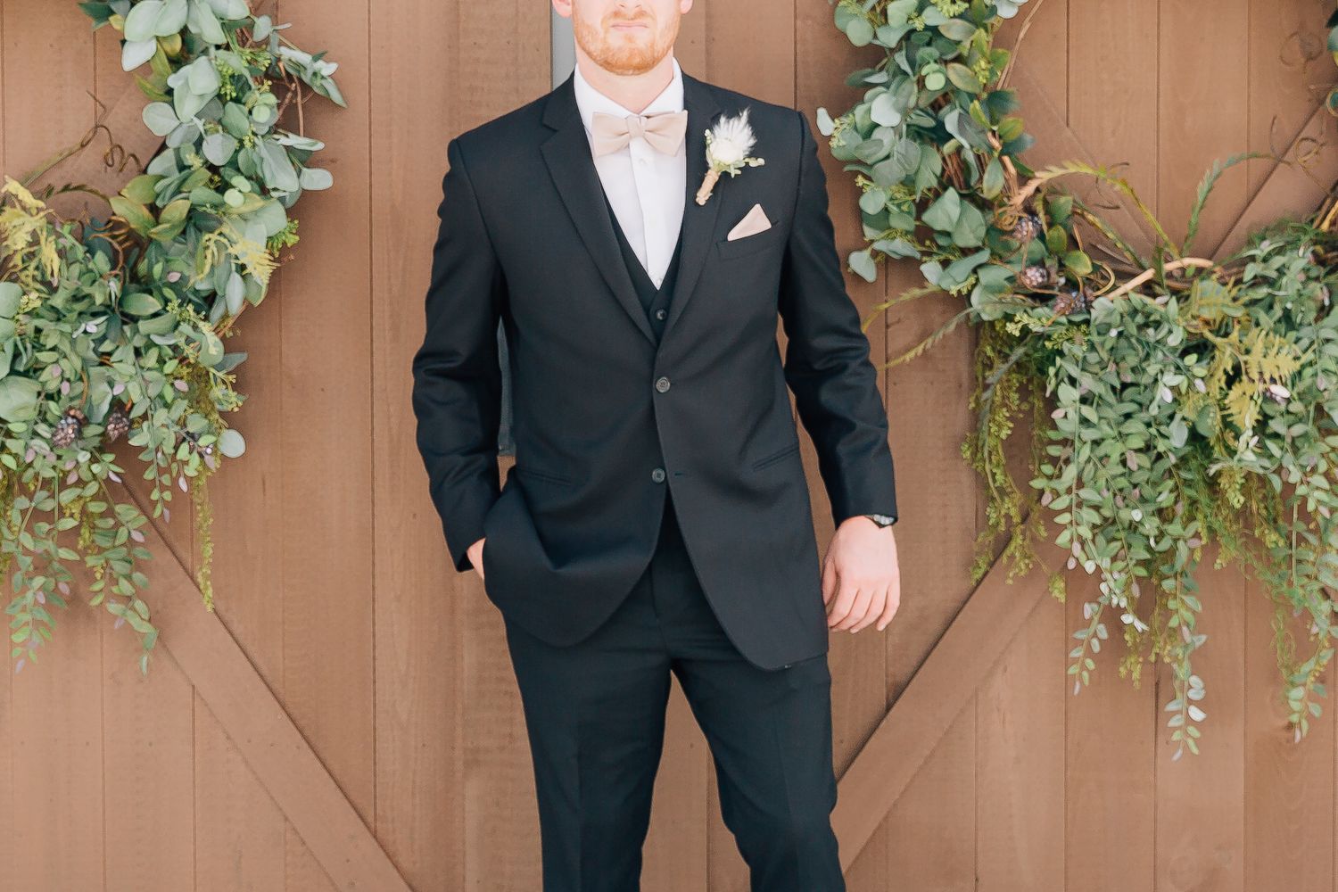 Classic black tuxedo with light grey tie and white boutonniere against wooden barn door.