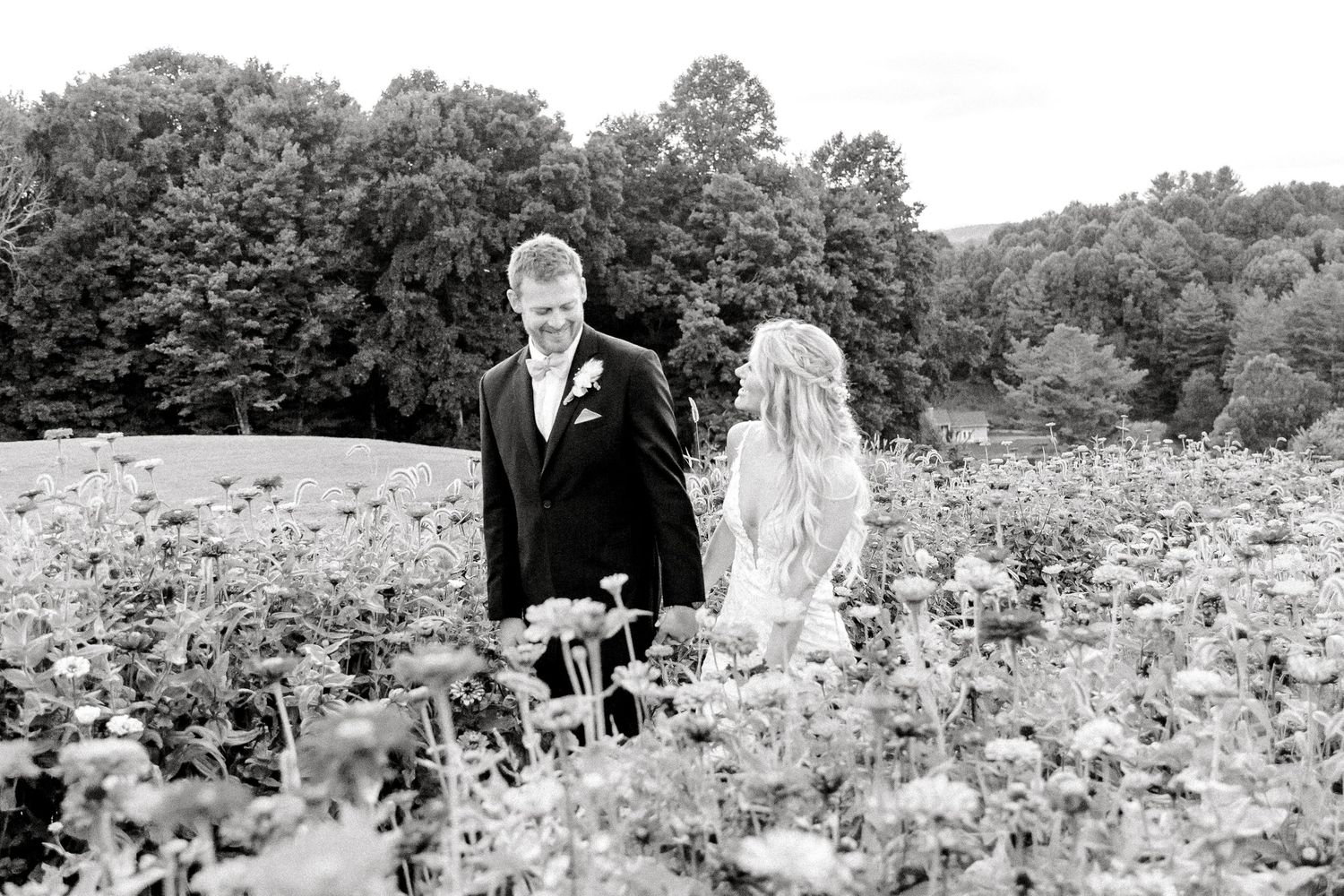 Black and white photo of a couple walking through a wildflower field on their wedding day.