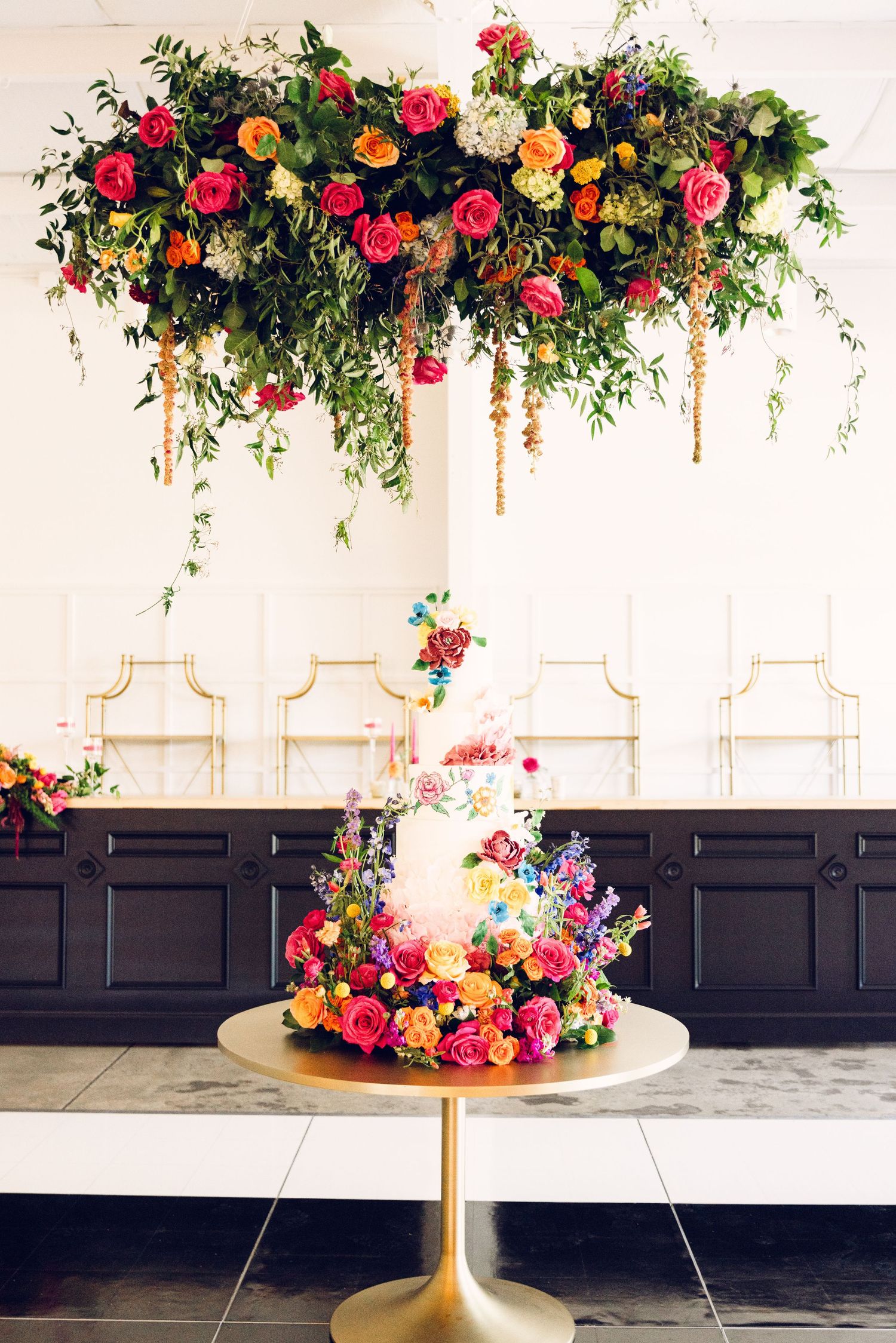 Gold pedestal table adorned with lush pink and orange floral arrangements against dark wainscoting.