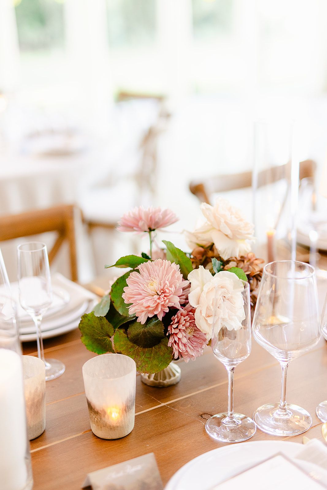 Elegant wedding reception table setting with pink dahlias and white roses in small vases alongside wine glasses.