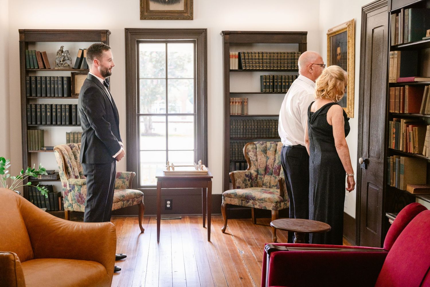 A couple practices their first dance in an elegant library setting with dark wood bookshelves and natural lighting.