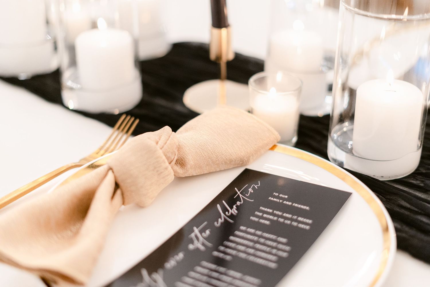 Elegant table setting with black tablecloth, beige napkins, and white candles creating an intimate atmosphere.