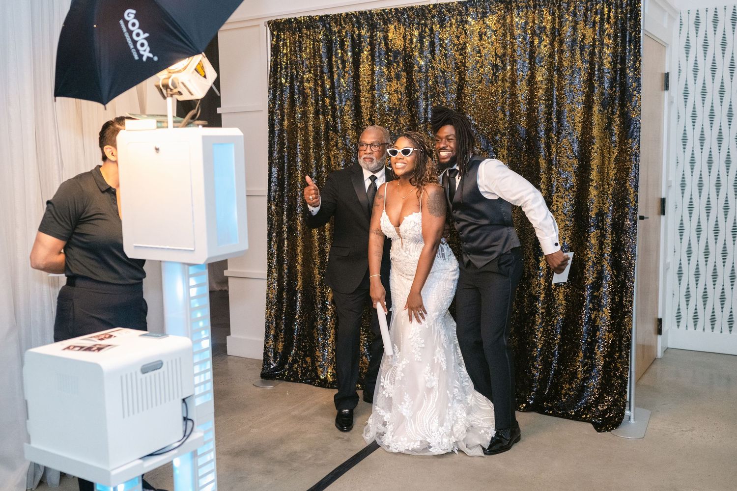 Wedding reception setup with gold sequin backdrop and white decor elements.