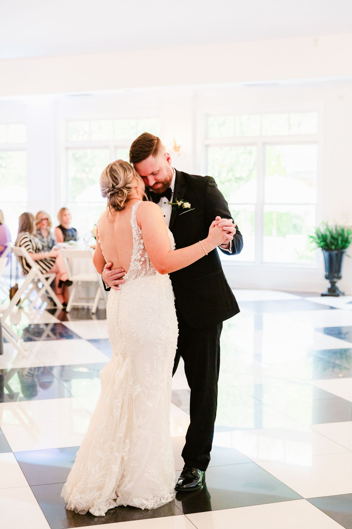 A couple shares their first dance at a wedding reception in an elegant white ballroom with natural lighting.