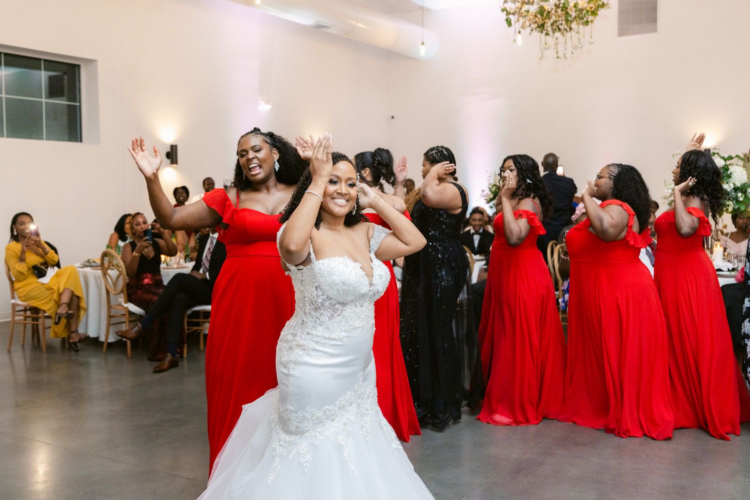 Wedding celebration in elegant white venue with red-dressed bridal party and guests dancing.