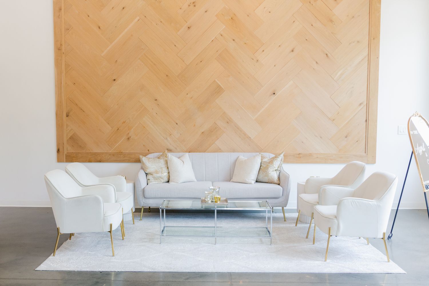 Modern white living room with herringbone wood wall panel and minimalist furniture arrangement on concrete floor.