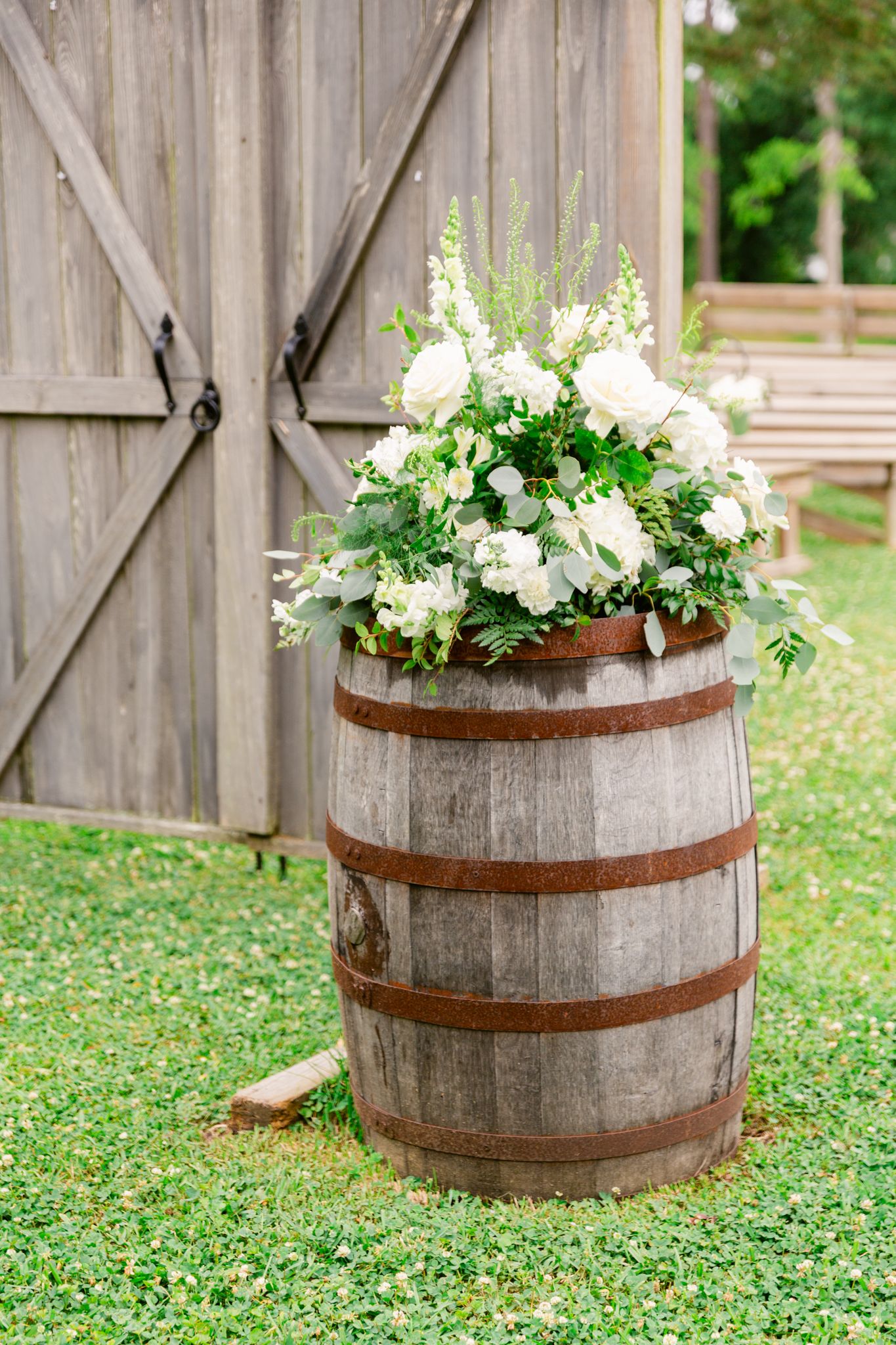 Rustic wooden barrels decorated with white floral arrangements create elegant outdoor wedding decor.
