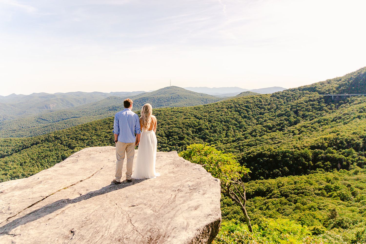 Two people stand on a rocky overlook enjoying sweeping mountain views on a sunny day in nature.