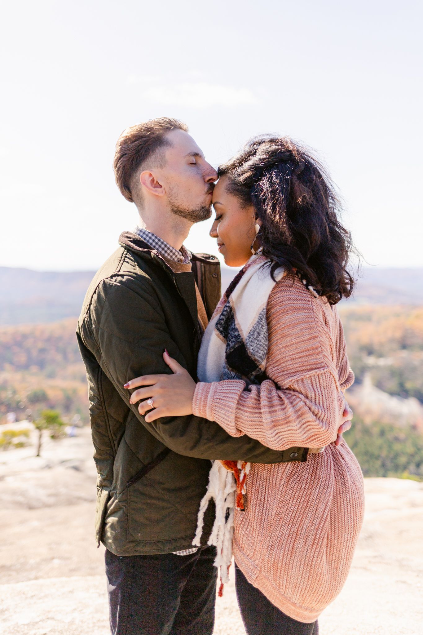 A tender moment shared between a couple on a scenic mountain overlook with sweeping valley views.