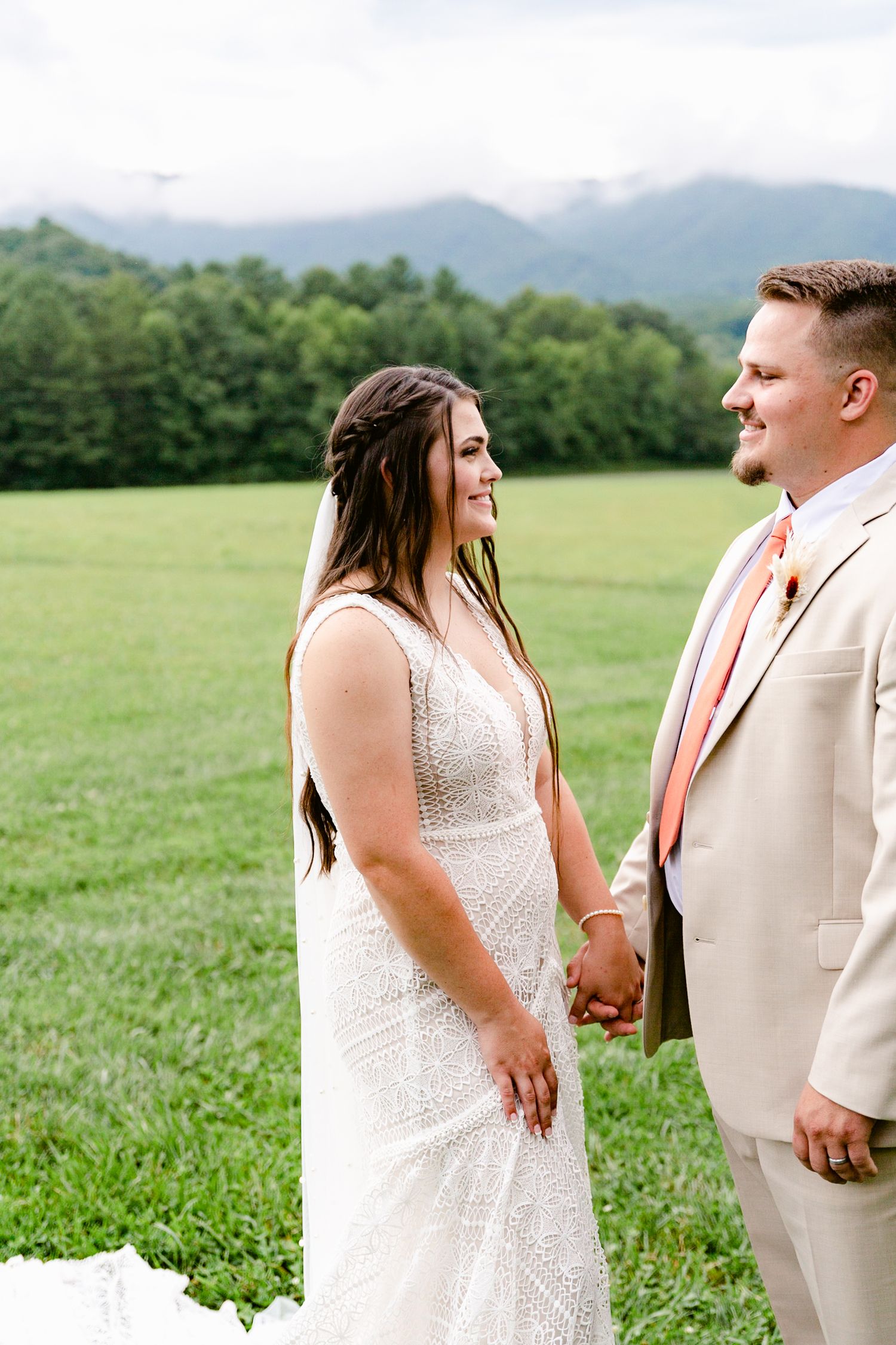 A couple shares a joyful moment together in a green field with mountains in the background.