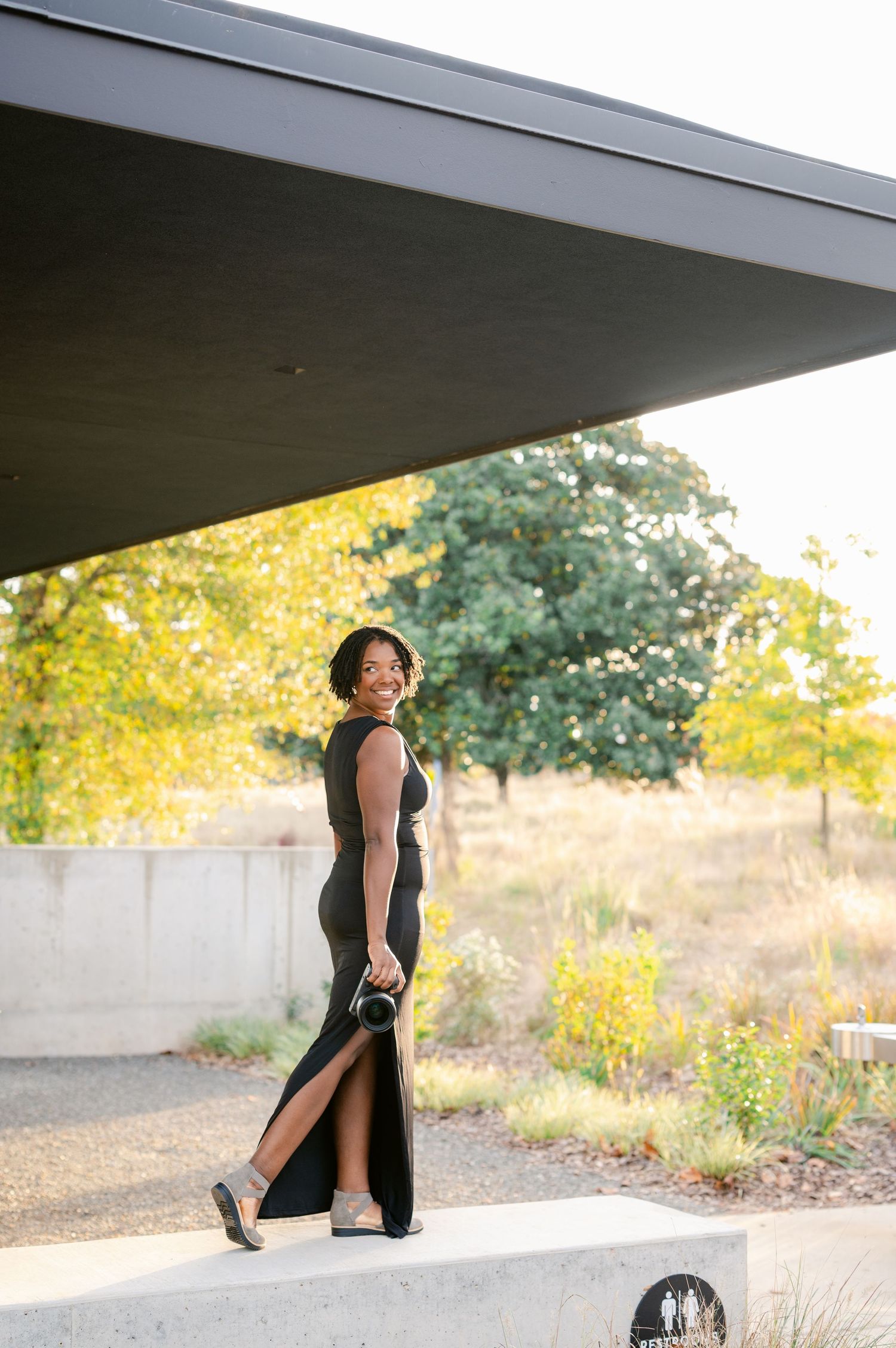 A dancer in black performs graceful movements under an architectural overhang at sunset.