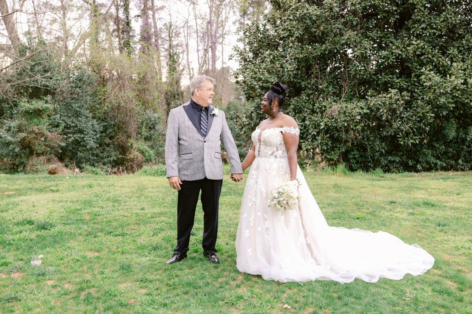 A couple in wedding attire walks through a lush garden setting during their outdoor photo session.