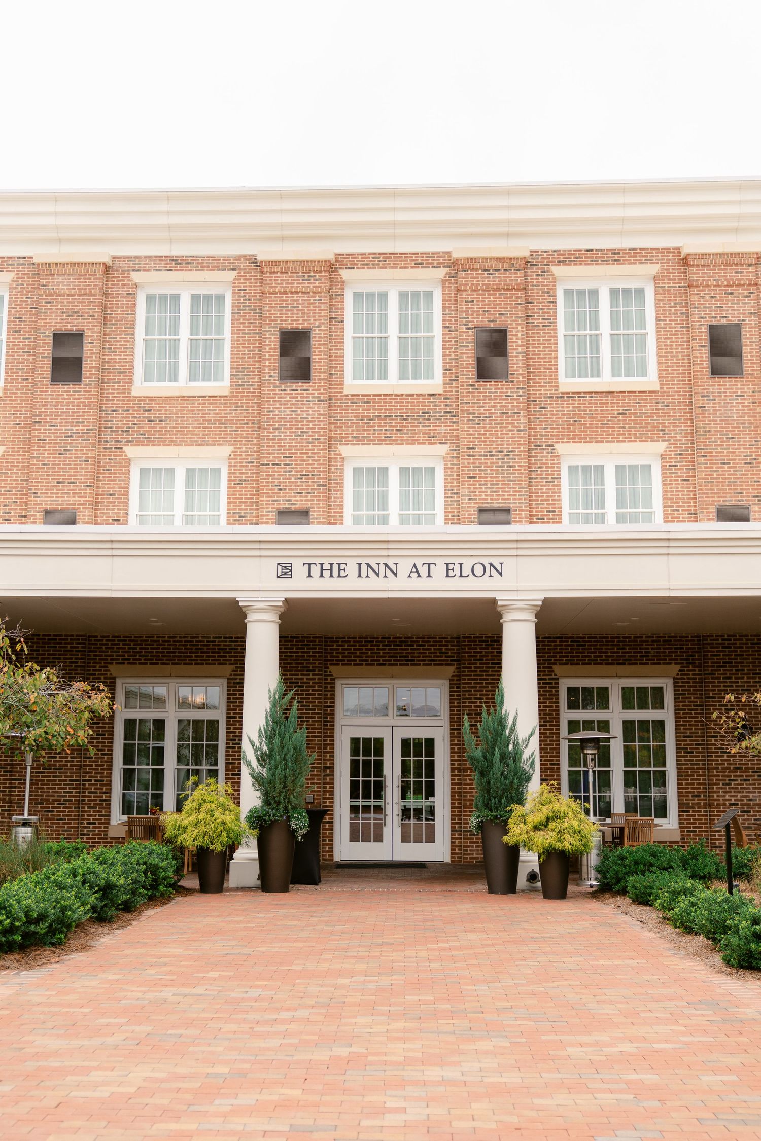 Exterior view of The Inn at Elon showing red brick facade with white columns and landscaping.