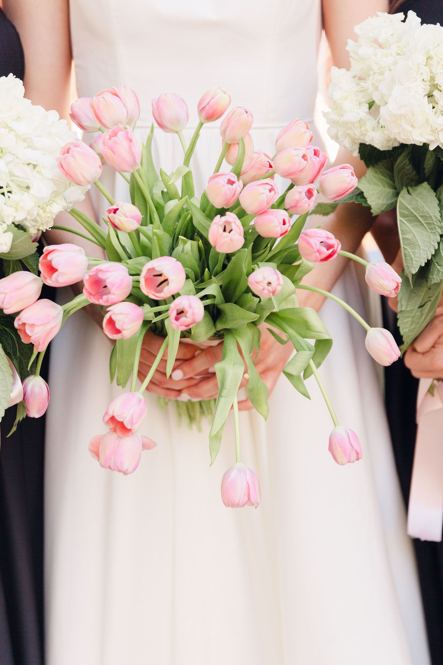 Pink tulips and white flowers create an elegant bridal bouquet line against a light background.