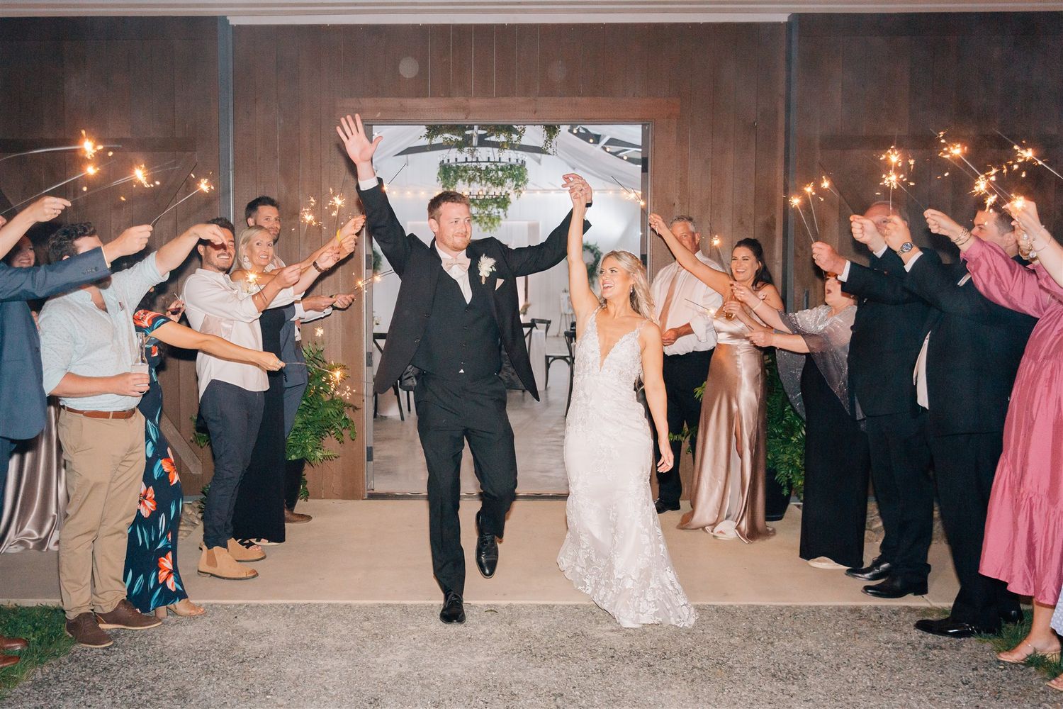 Newlyweds make a grand exit through a tunnel of guests holding sparklers at night.