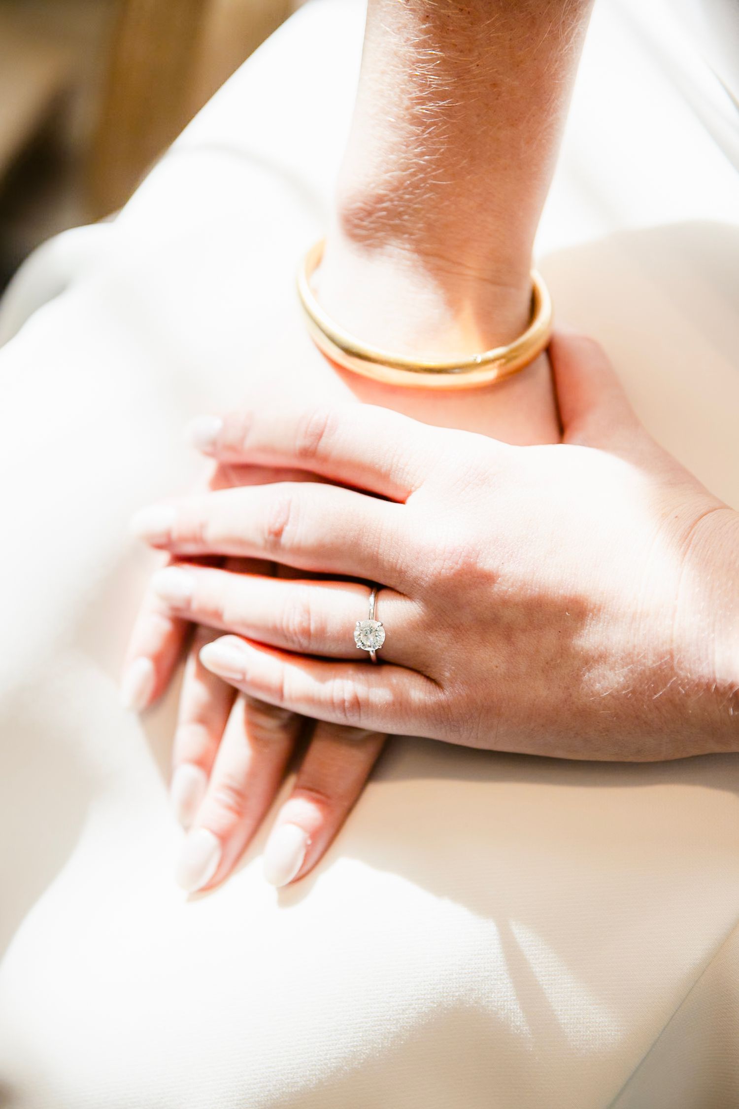 Close-up shot of hands wearing wedding rings resting on white fabric.