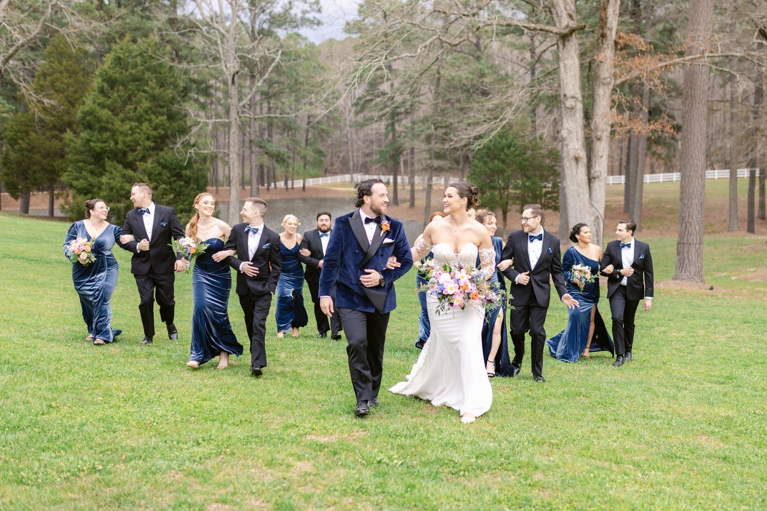 Wedding party walking and celebrating on grass with trees in background.