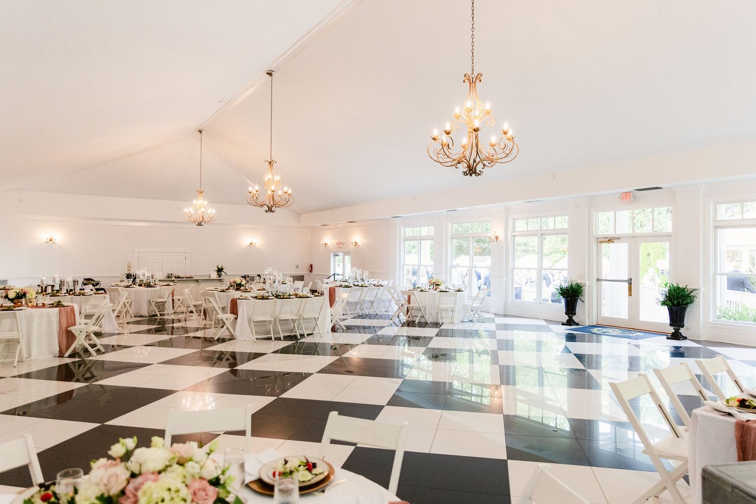 Elegant wedding reception venue with black and white checkered floor, crystal chandeliers, and white tables.