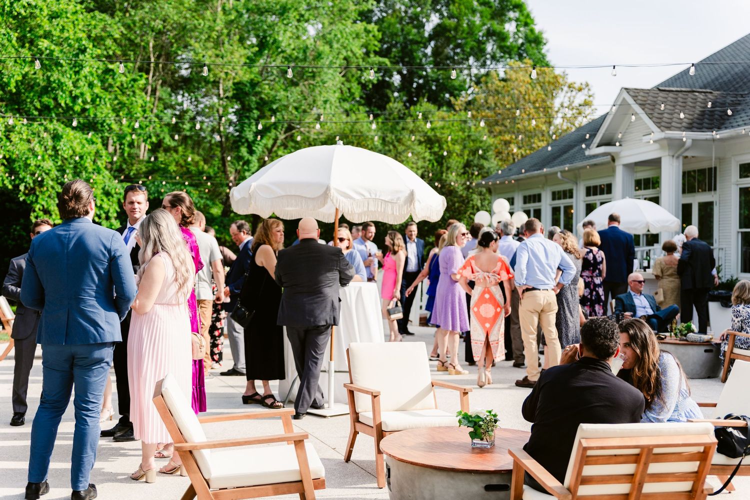 Wedding guests mingle outdoors at an elegant garden reception with white tents and peach-colored decor.