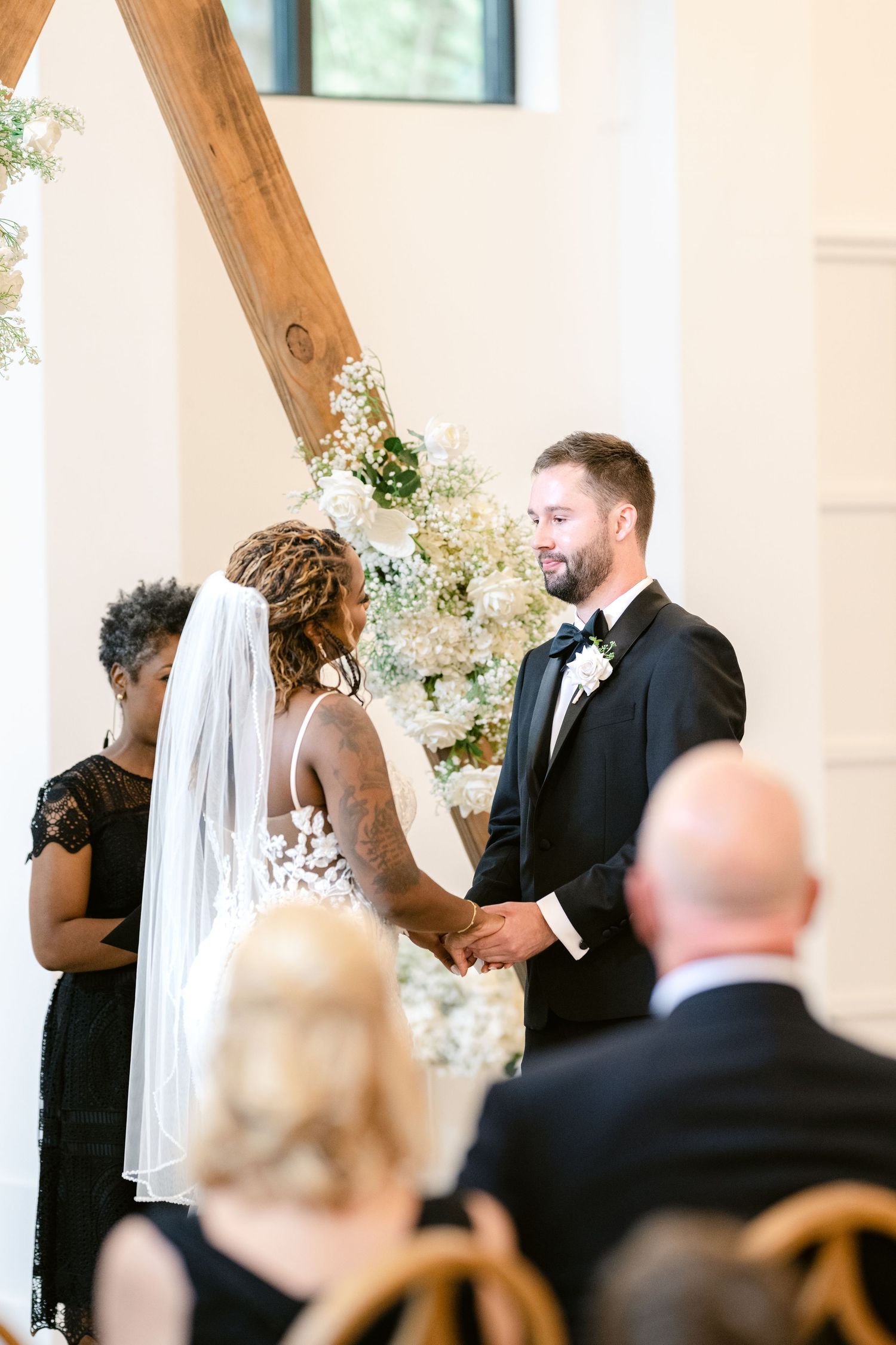 Wedding ceremony in progress inside an elegant venue with exposed wooden beams and natural light.