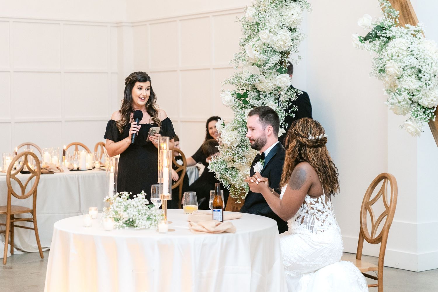Wedding celebration with guests seated at an elegant table decorated with white floral arrangements and gold chairs.