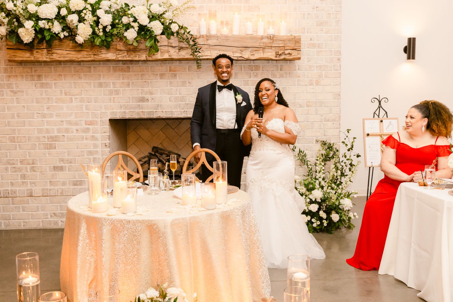 Elegant wedding reception setup with white floral arrangements and brick wall backdrop.