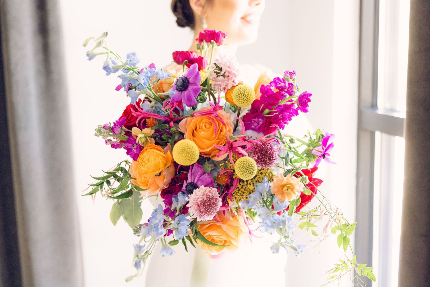 Bright and colorful floral arrangement with roses, delphiniums, and mixed blooms.