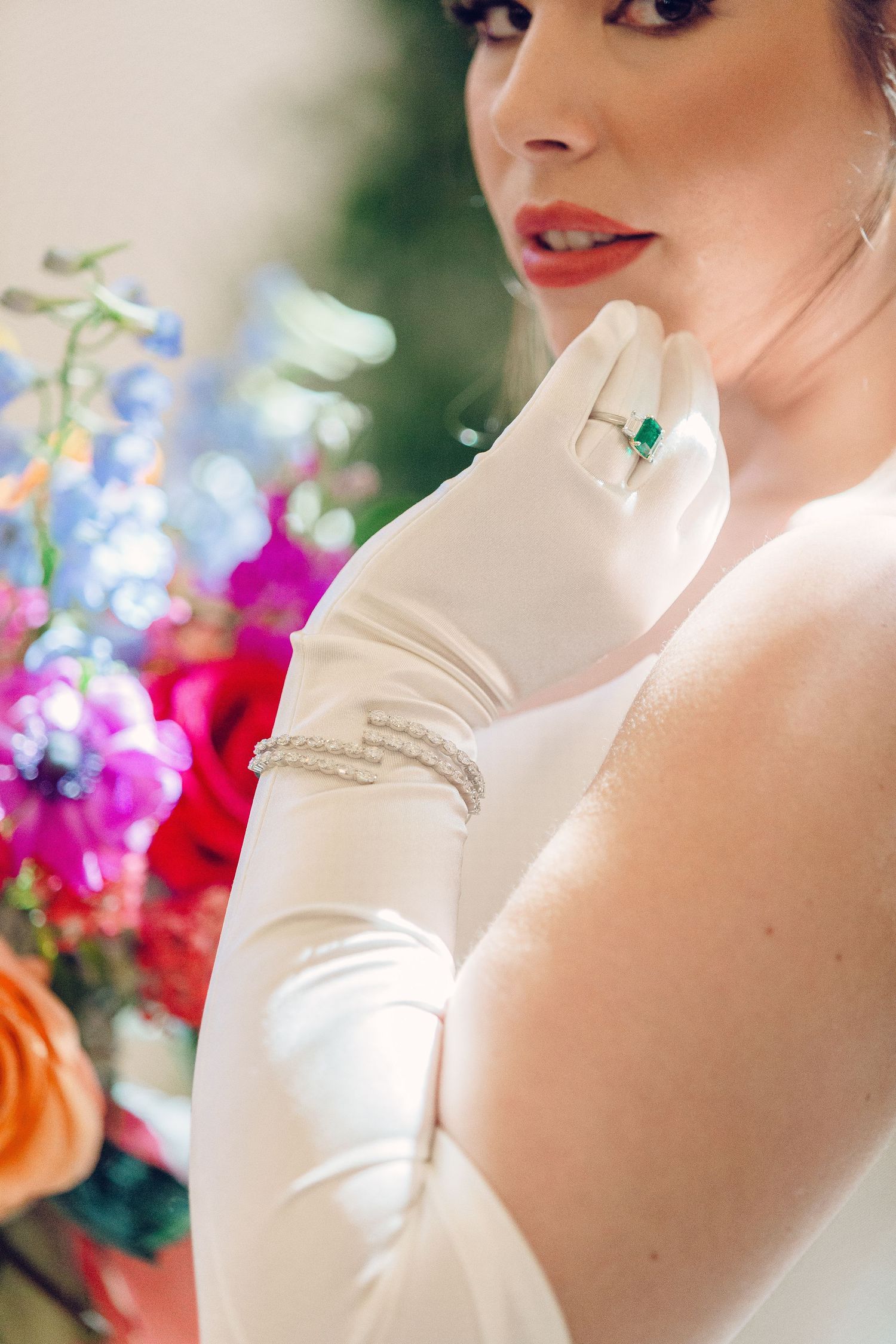 Elegant white bridal gown with vibrant colorful floral bouquet against a blurred garden background.