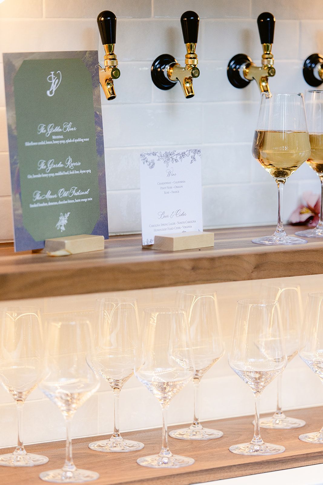 Row of wine glasses and tasting cards displayed on illuminated white shelf at an event.