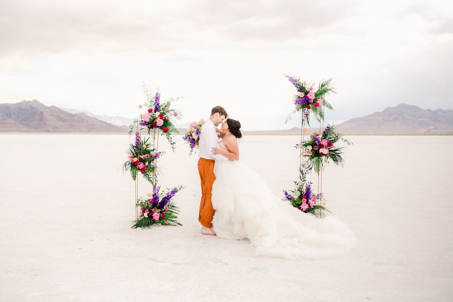 A couple embraces under a floral arch on the salt flats with mountains in the background.