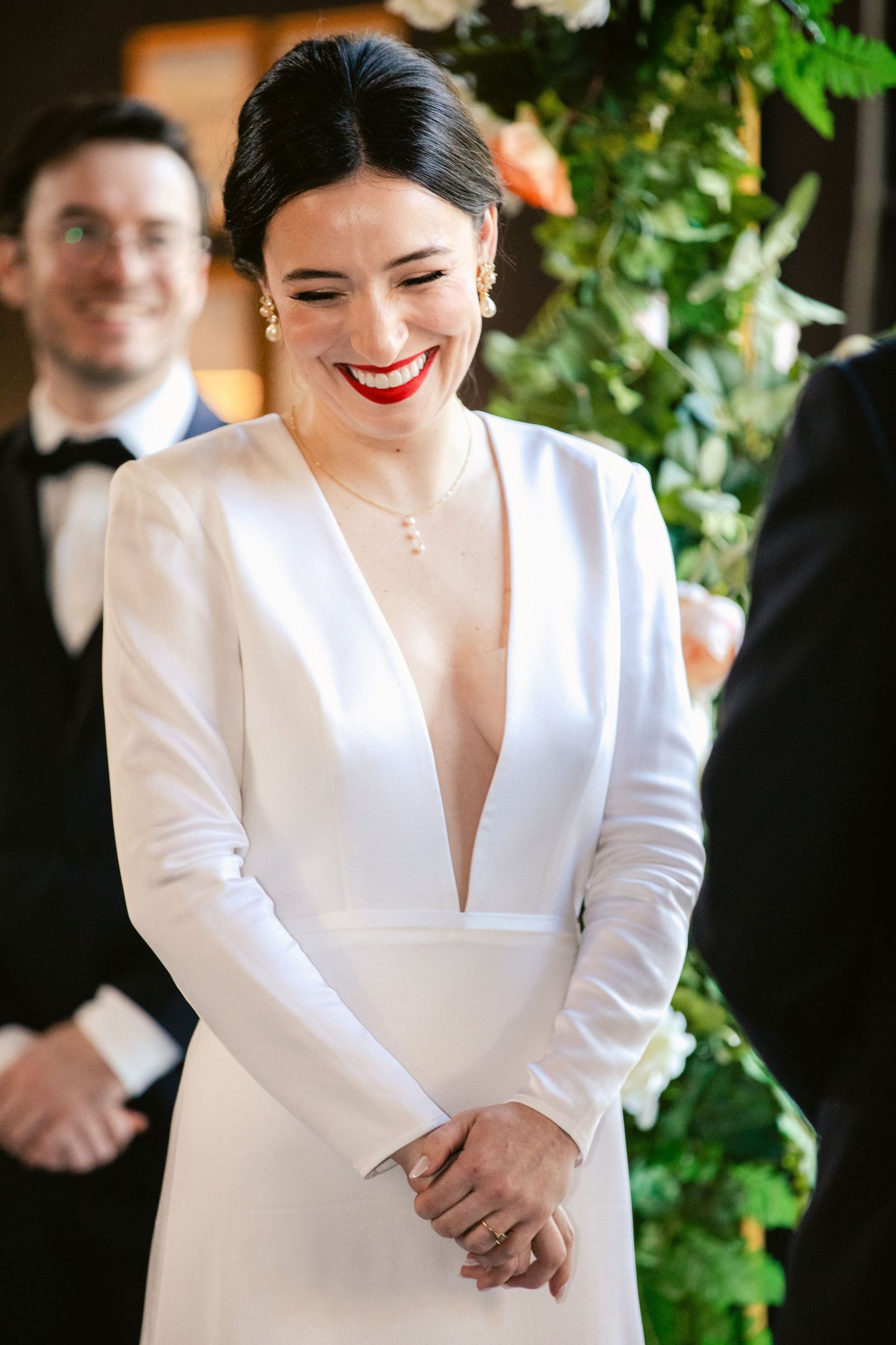 A bride in a modern white long-sleeved gown smiles during her wedding celebration.