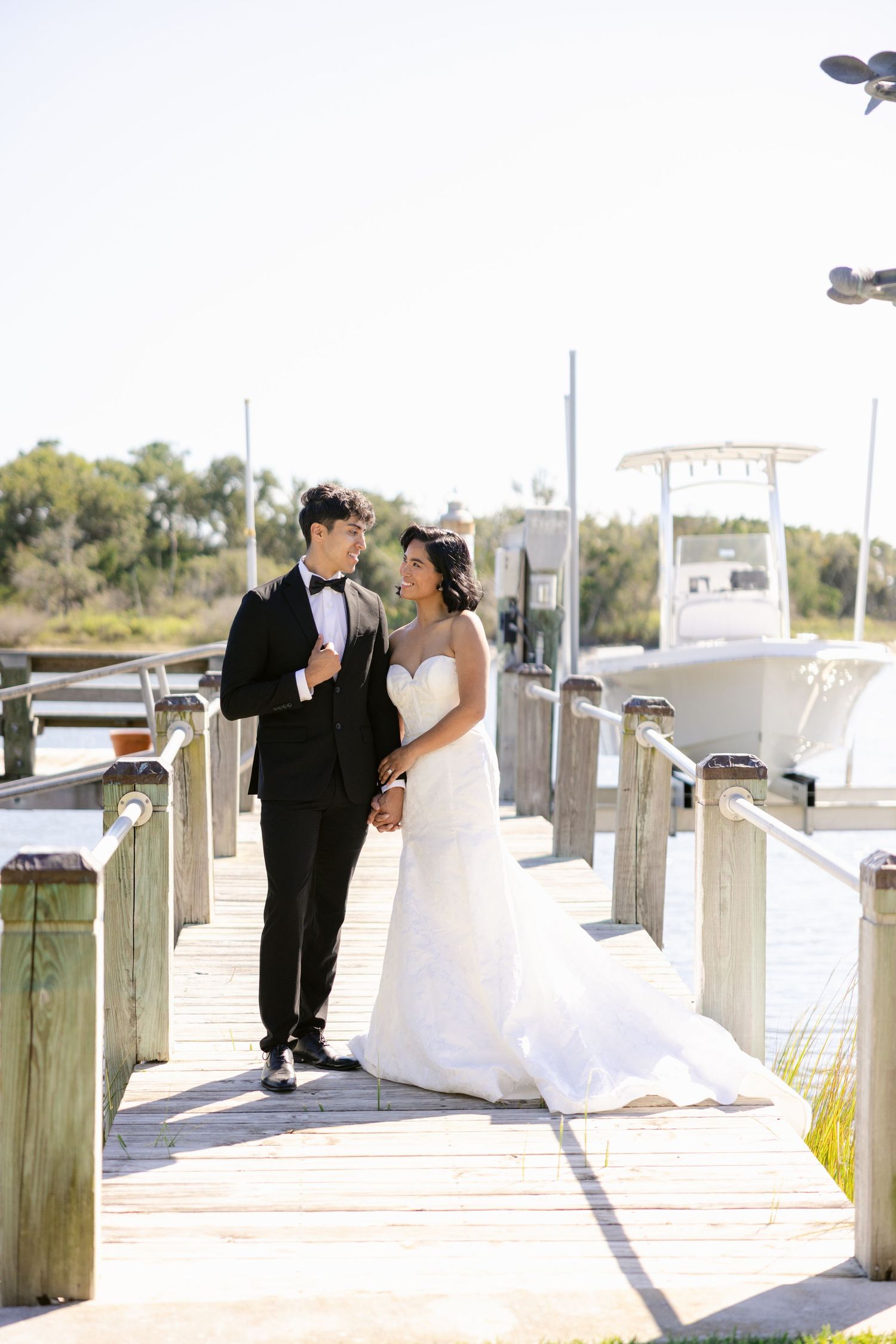 Romantic waterfront dock scene with elegant wedding attire and boats in the background.