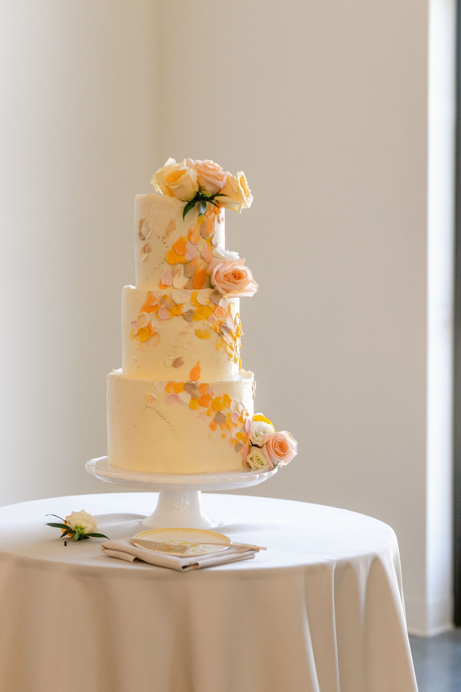 Elegant wedding cake with peach-colored flowers and delicate decorations on a white tablecloth.