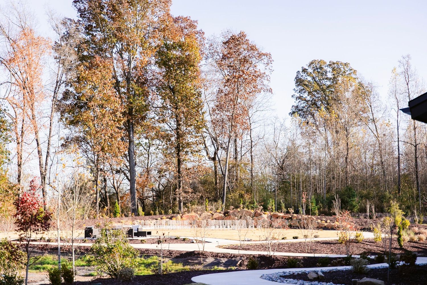 A scenic autumn landscape with tall trees and stone landscaping features around a garden pond or water feature.