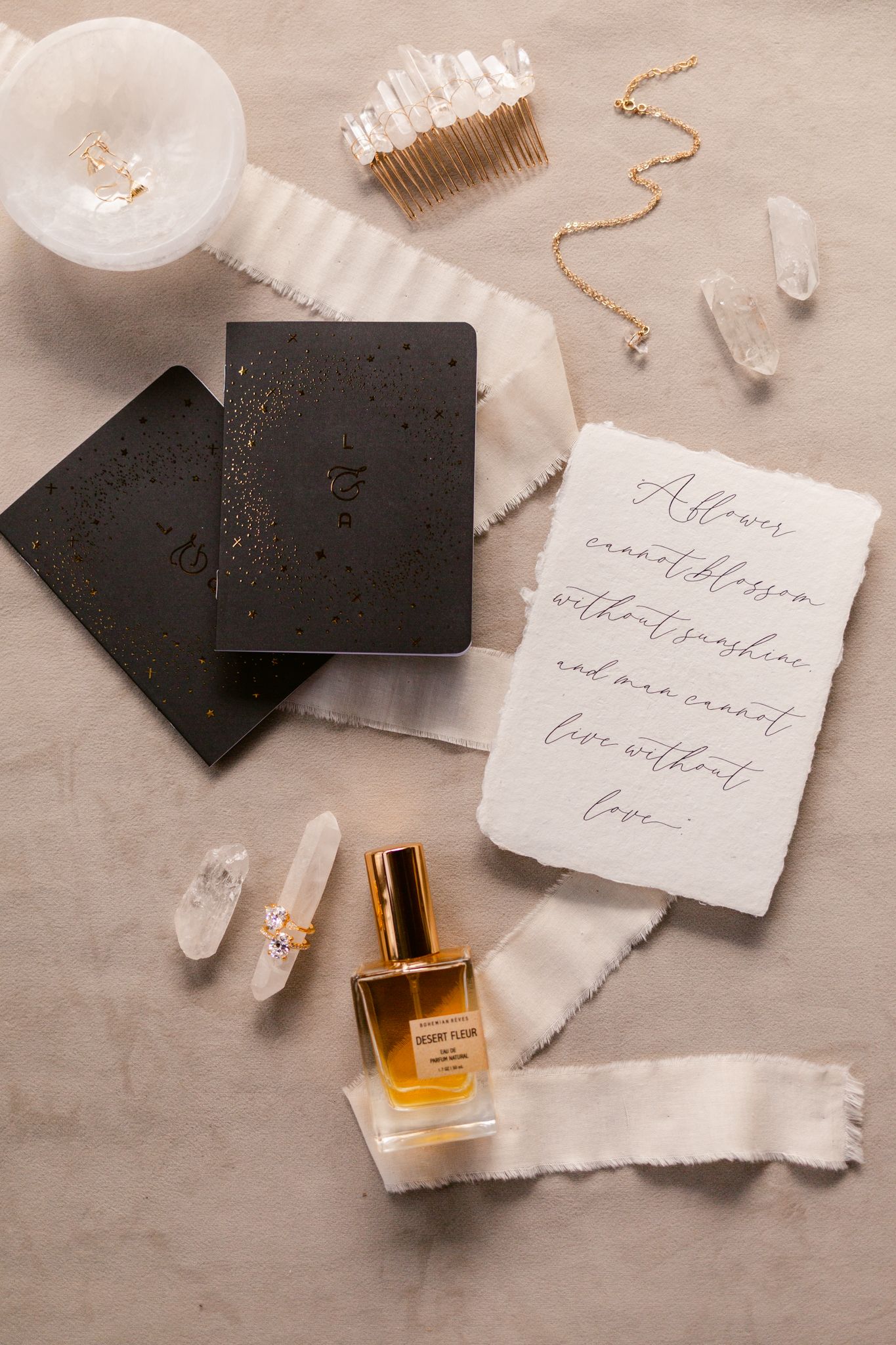 Wedding stationery flatlay with black cards, perfume bottle, and handwritten calligraphy on beige background.
