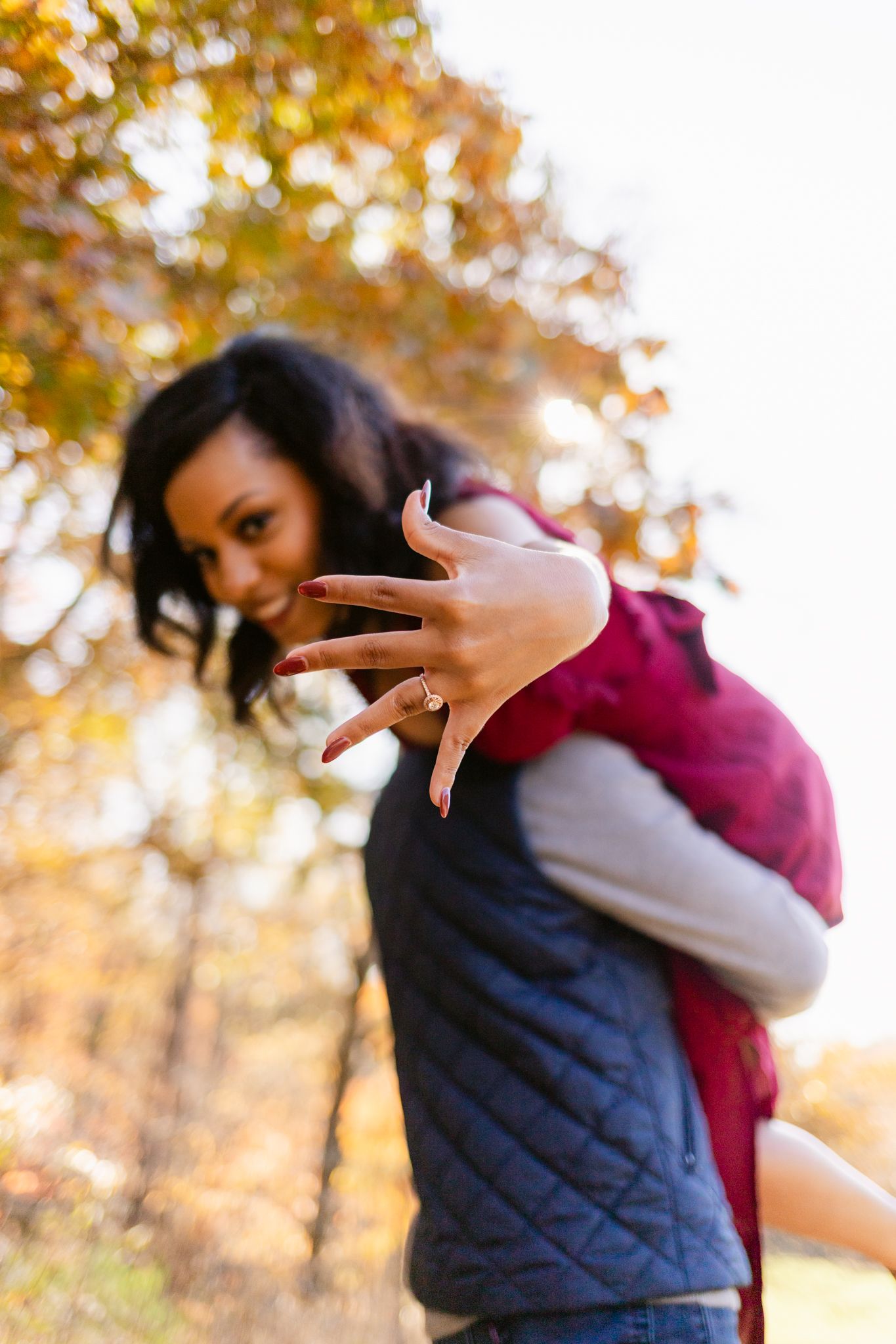 Playful autumn portrait with navy quilted vest and burgundy sleeves against golden fall foliage in background.