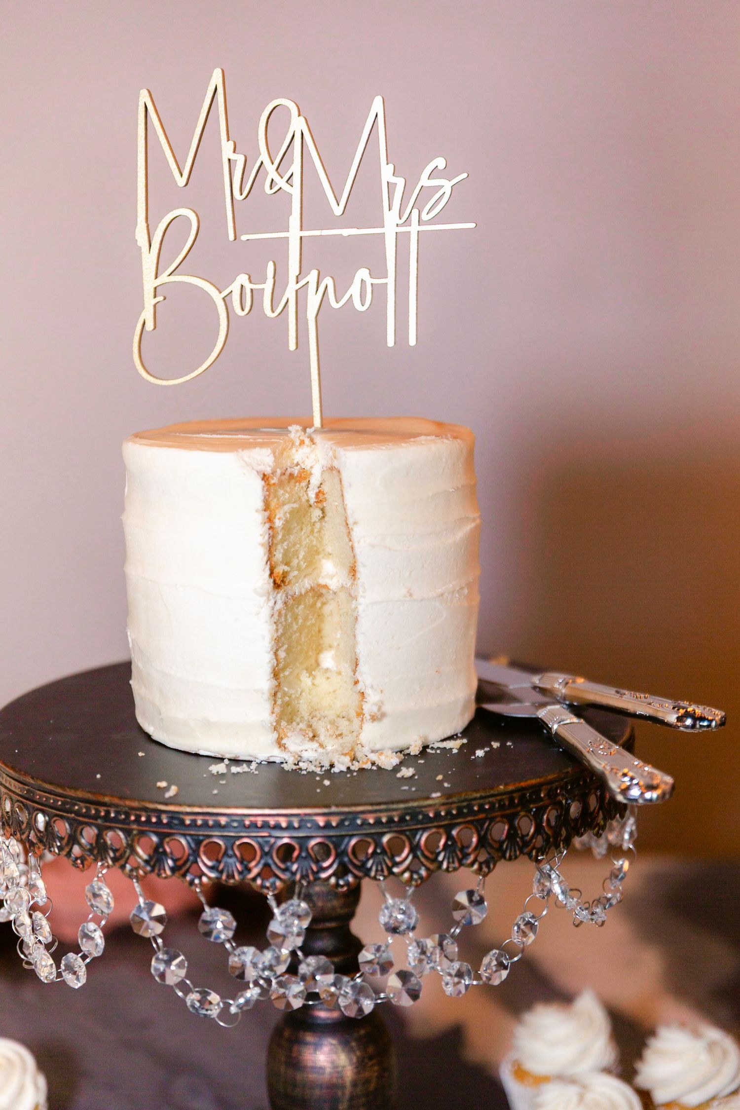 White wedding cake displayed on an ornate crystal-trimmed black cake stand.
