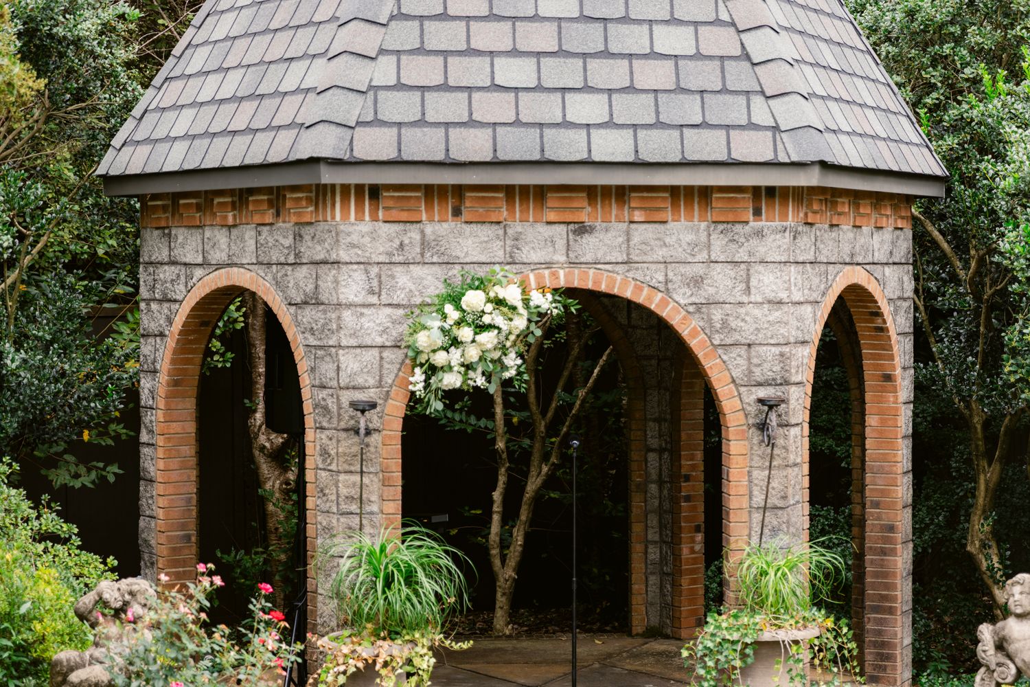 A series of elegant brick archways with stone accents create a covered walkway in a lush garden setting.