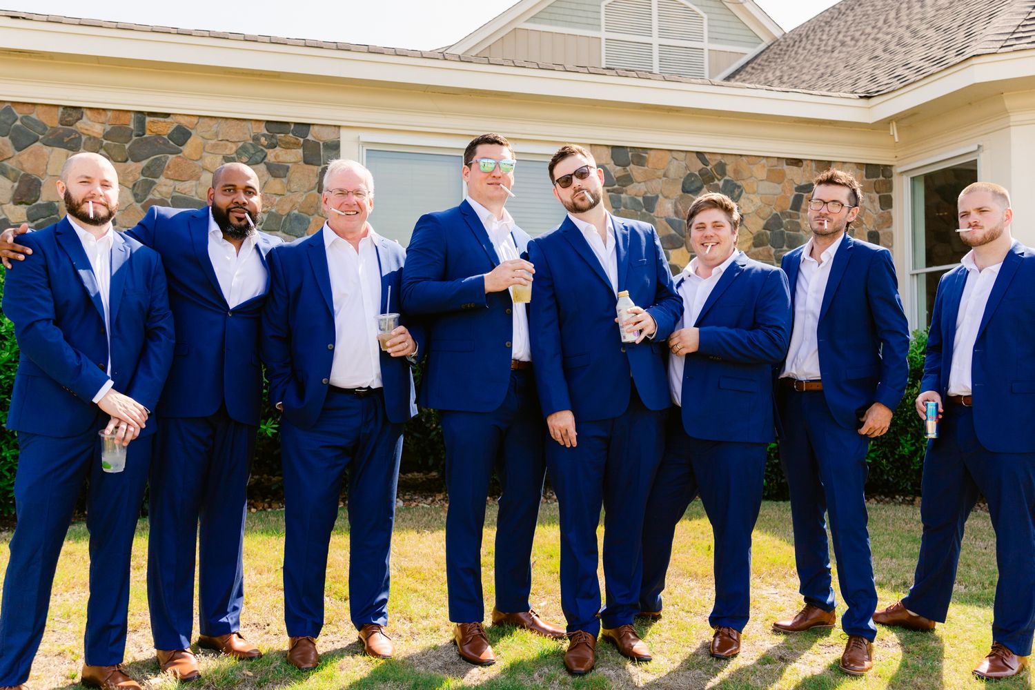 Wedding party in navy blue suits jumps in unison for a fun group photo outside a building.