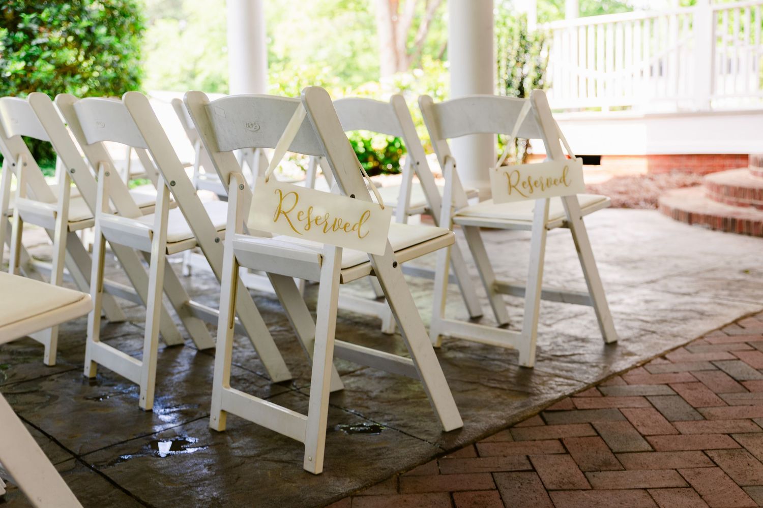 White folding chairs arranged in rows on a brick patio for an outdoor wedding ceremony.