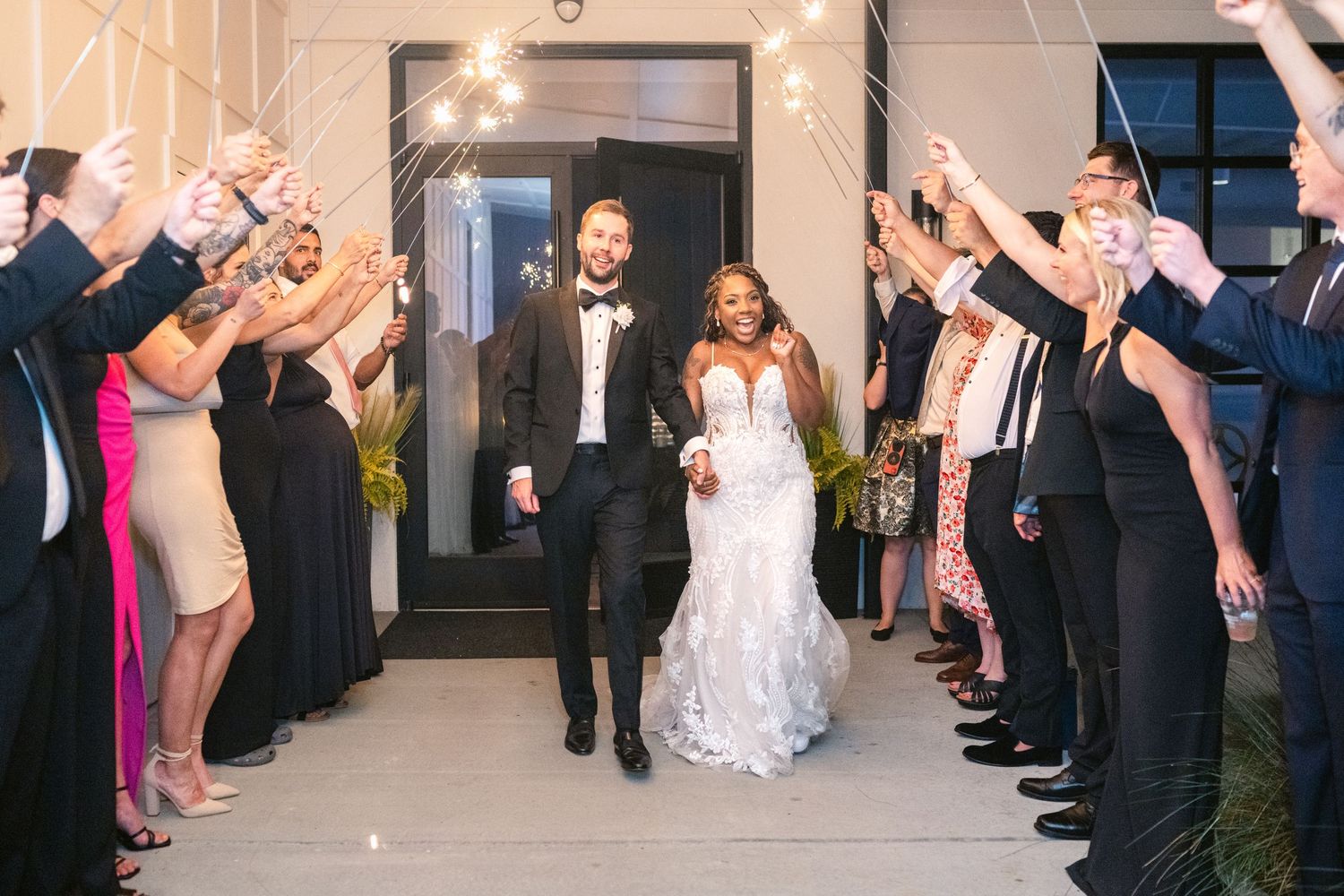 Wedding guests form an arch with sparklers as the newlyweds exit through the glowing tunnel at night.