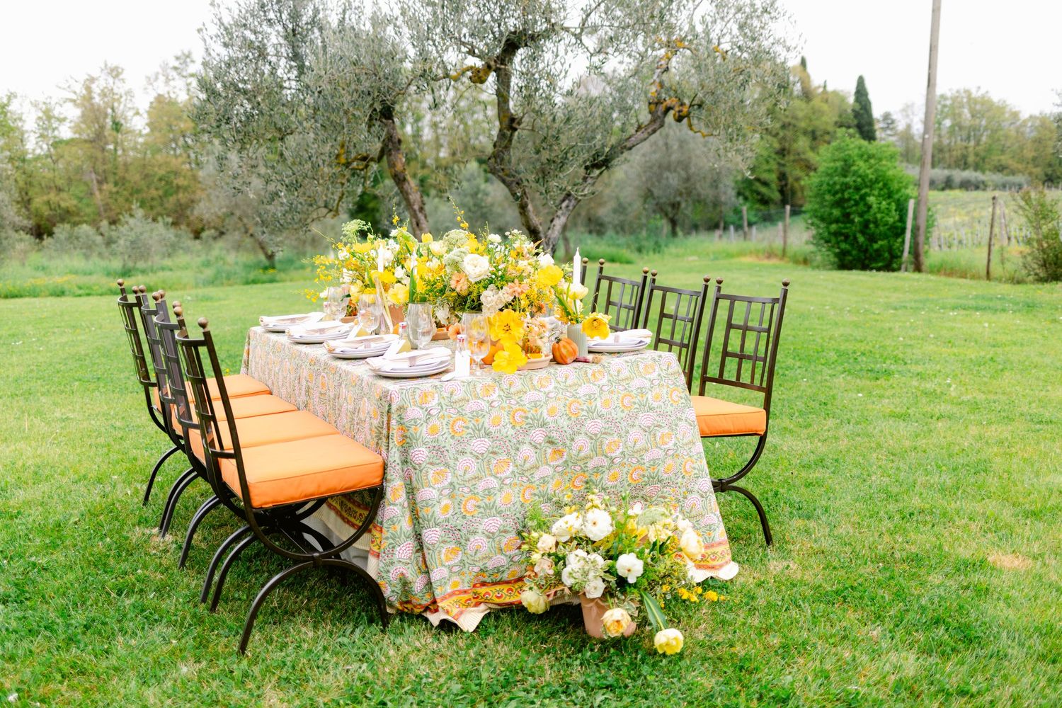 A series of outdoor dining tables with floral tablecloths and chairs set up on a grassy lawn for an elegant garden party.
