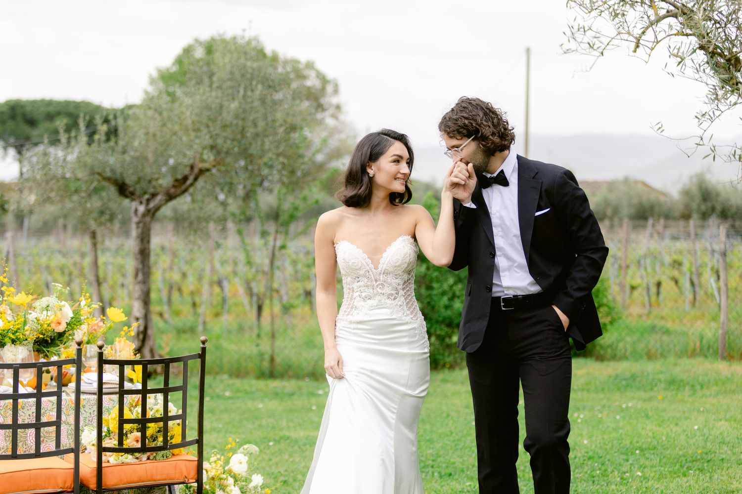 A couple shares a romantic moment in a vineyard garden with yellow flowers and greenery in the background.