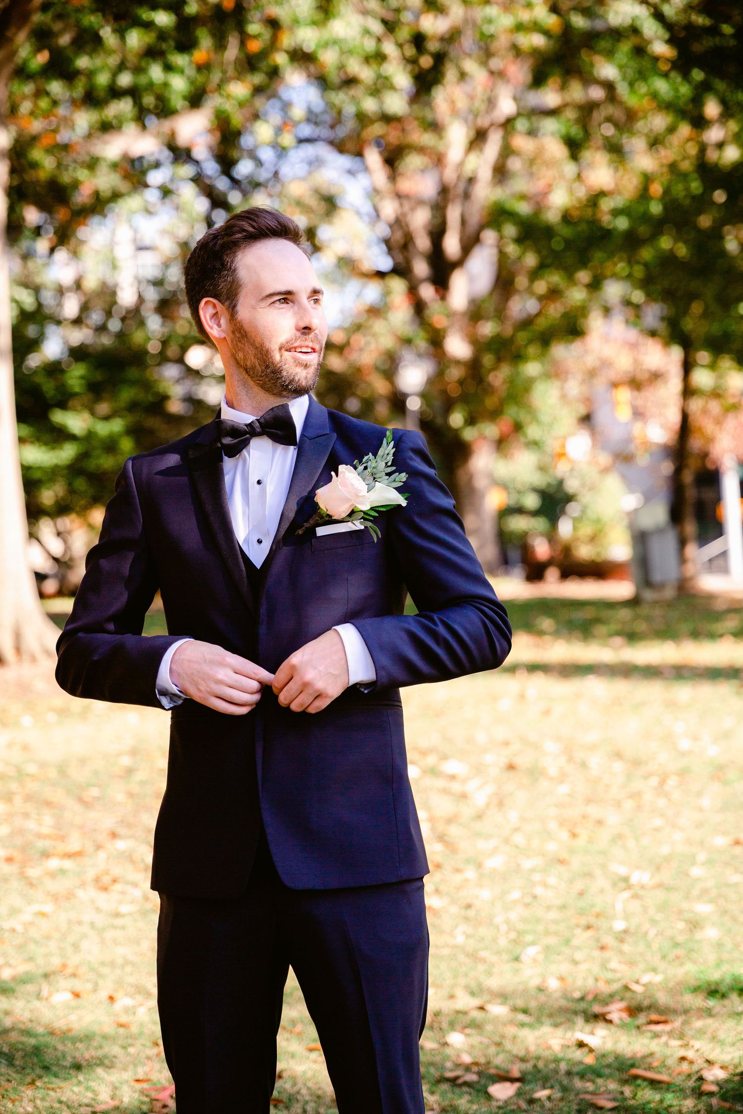 Two people in dark suits share a joyful moment together in an autumn park setting.