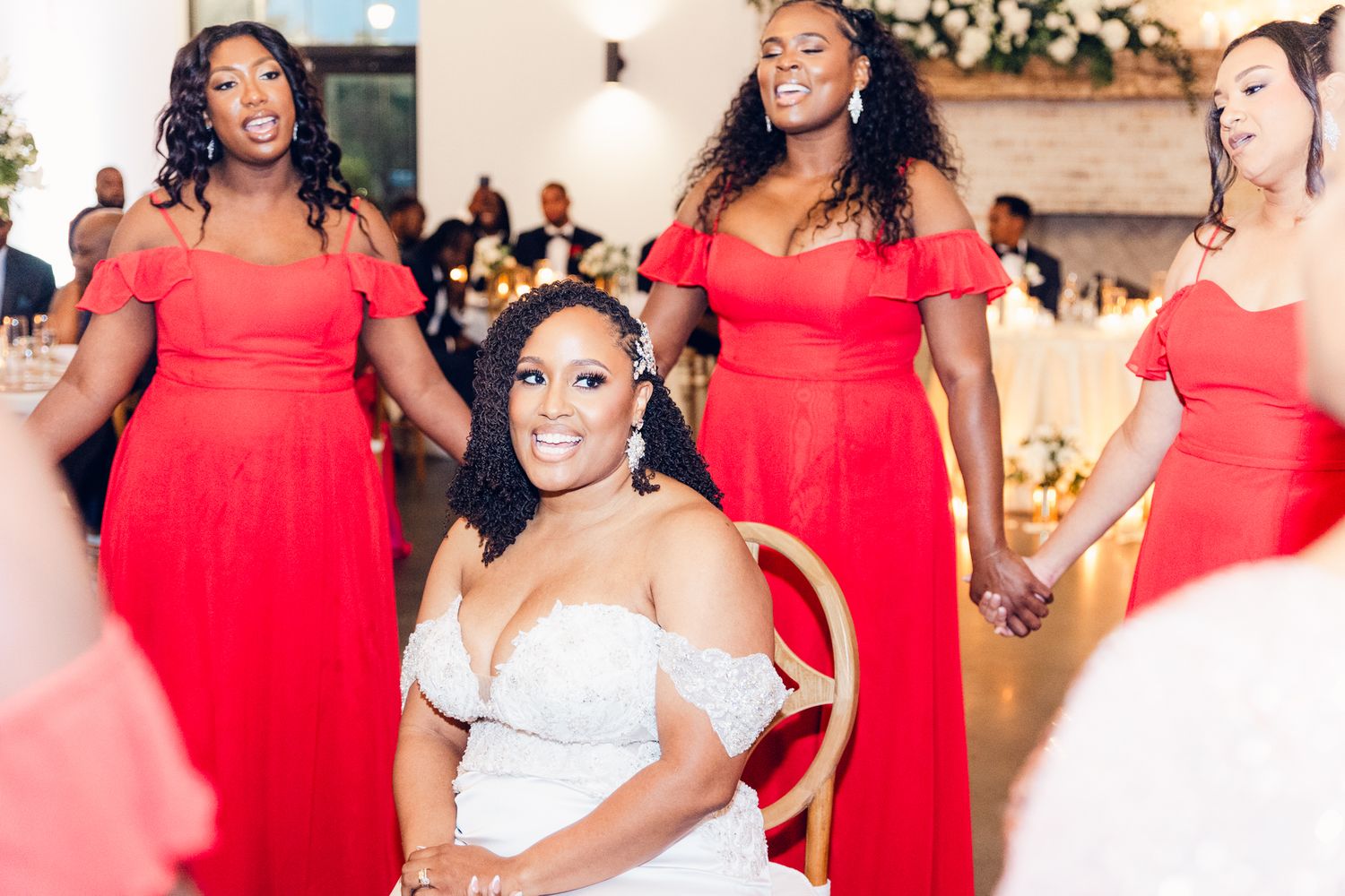 Wedding party members in bright red bridesmaid dresses pose together during celebration.