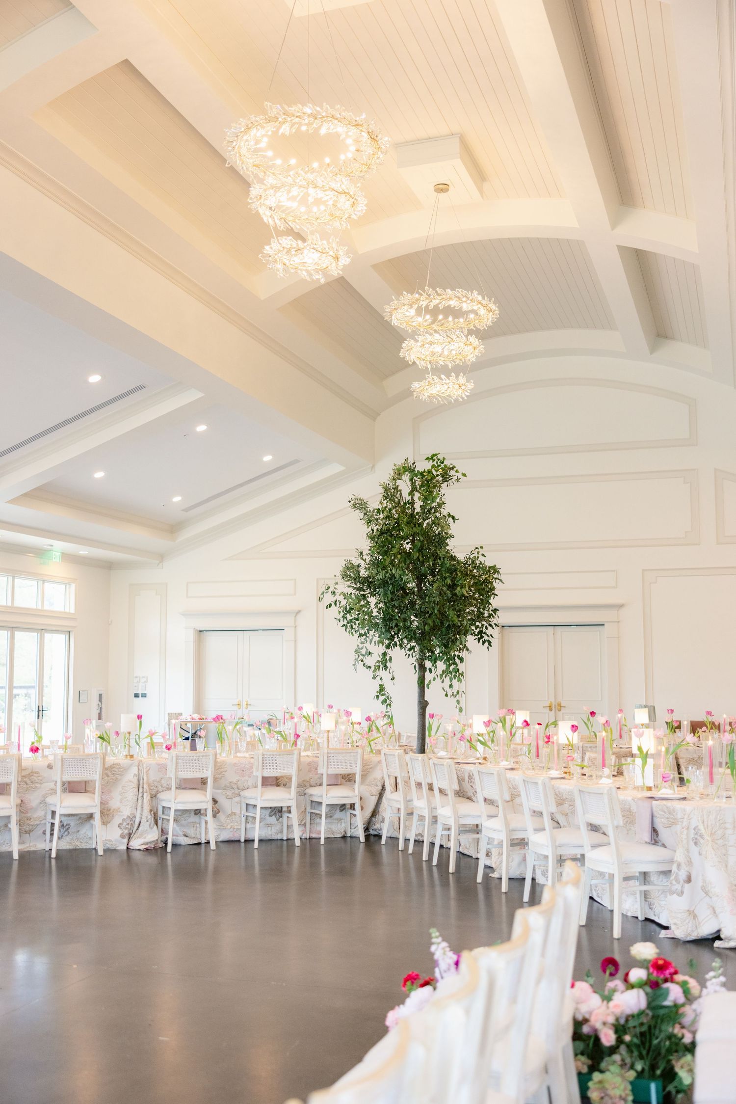 Elegant white wedding reception venue with crystal chandeliers and white chairs.