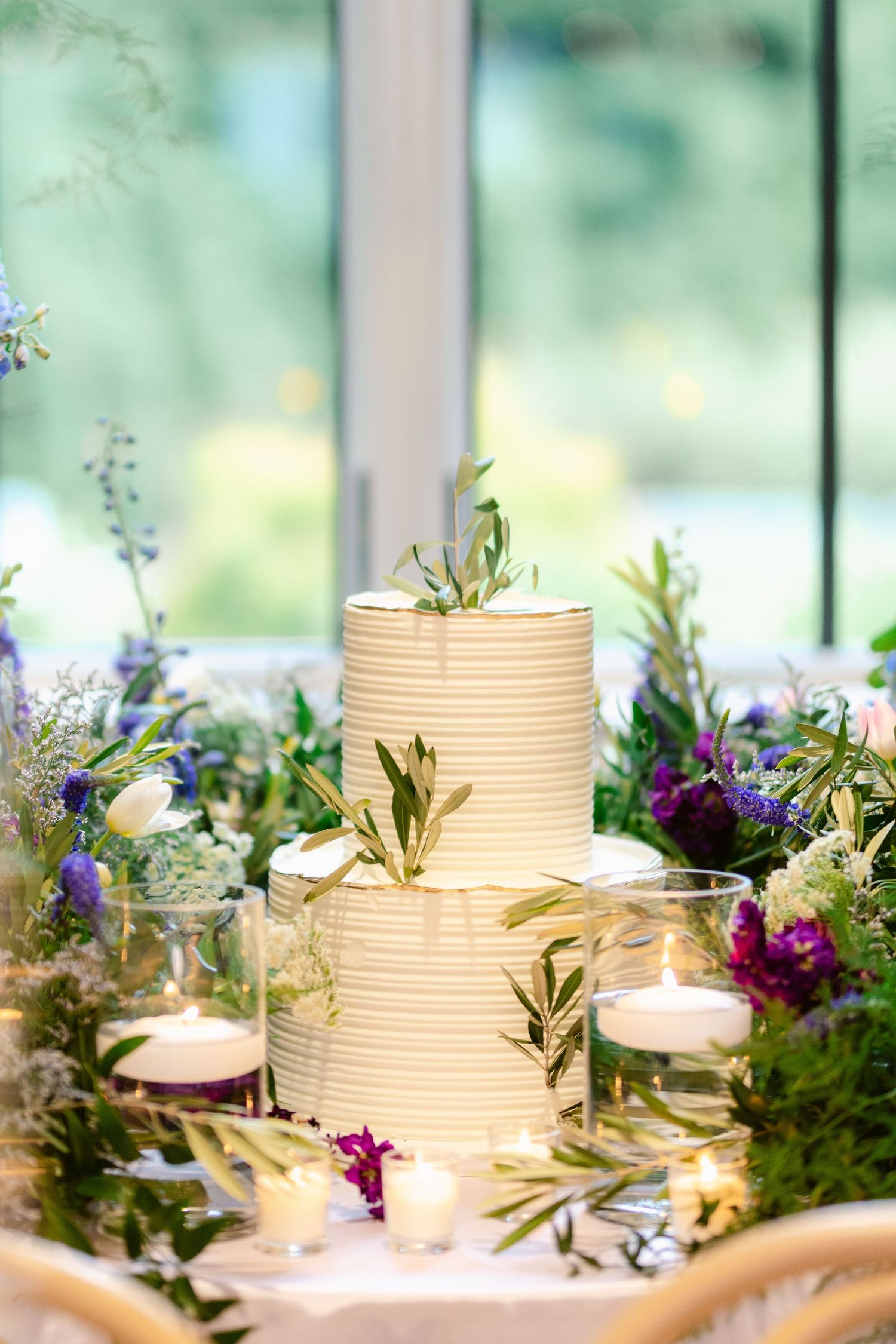 Elegant wedding cake display with purple and white flowers and greenery.