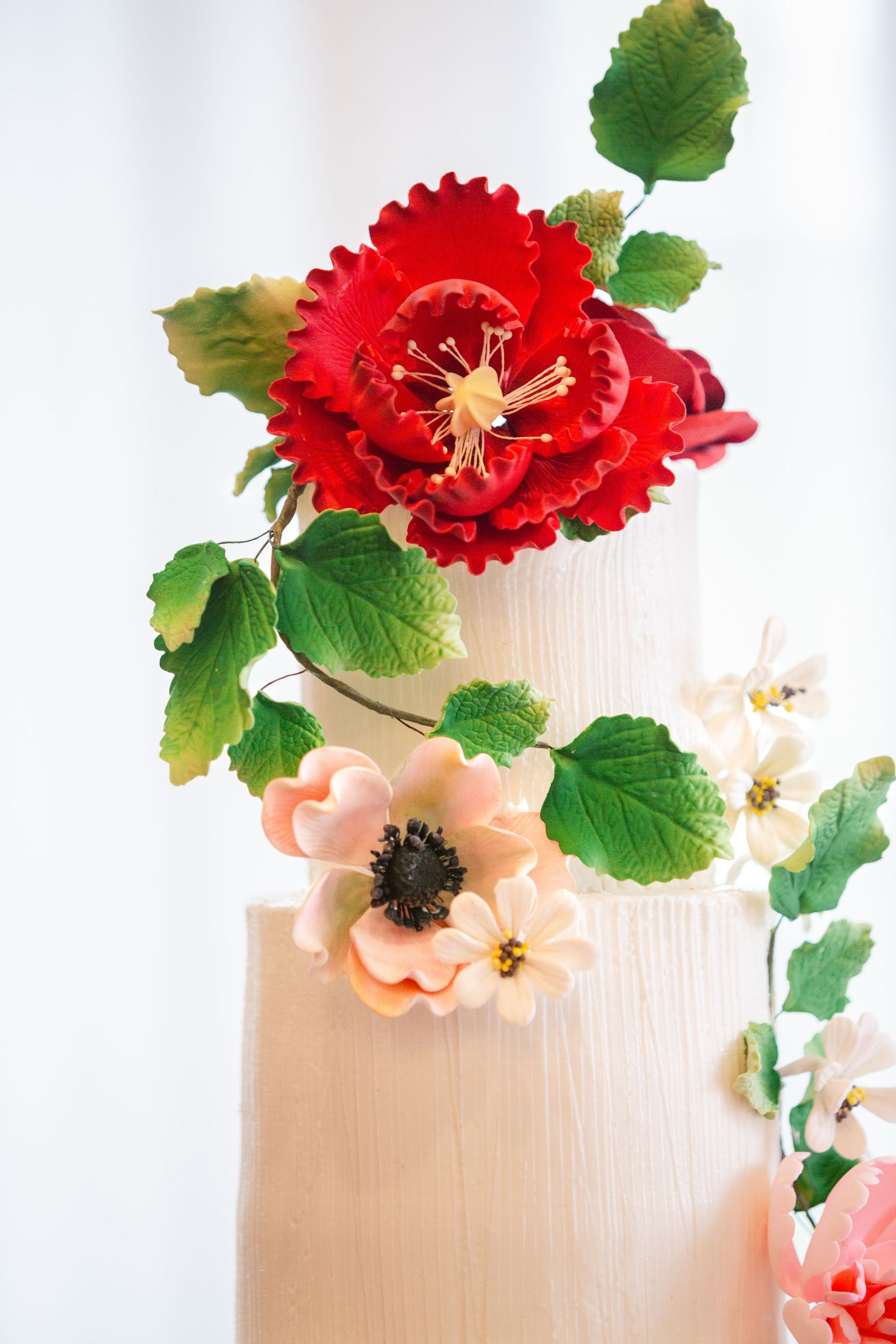 Vibrant red and pink artificial flowers with green leaves arranged against a light beige textured background.