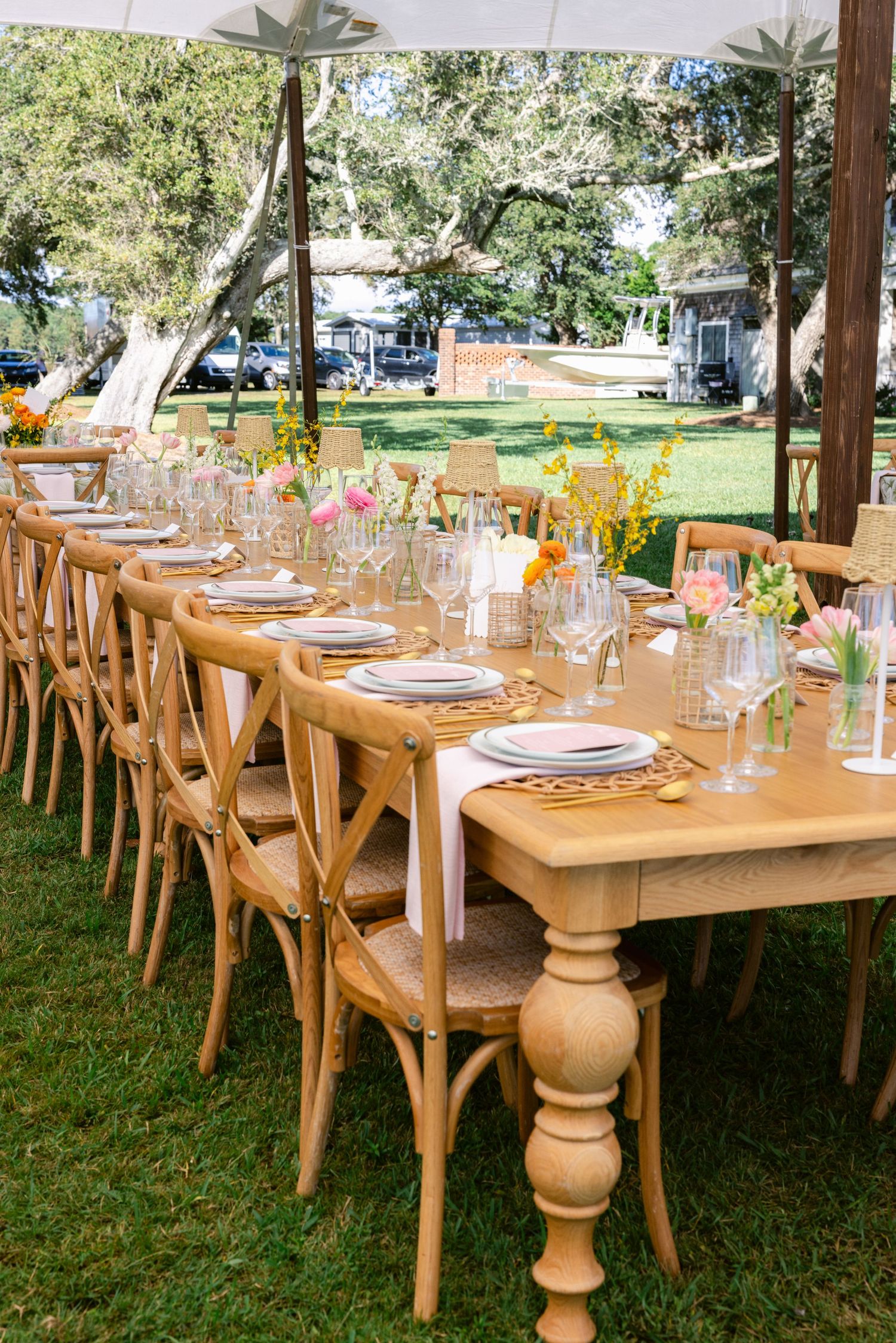 Long wooden farmhouse table with crossback chairs set for outdoor wedding reception.
